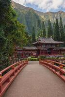 The Byodo In Temple on Oahu, Hawaii, features traditional Japanese architecture, a red bridge, manicured gardens, and mountains in the background. photo