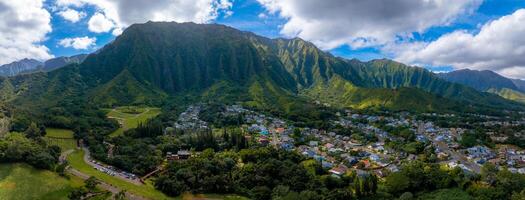 Aerial view of green mountains on Oahu island, Hawaii, with dense vegetation, a residential area, and a small temple like structure in the foreground. photo