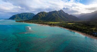 Aerial view of Oahu, Hawaii, showing turquoise waters, a sandy beach, and the lush Ko olau mountain range under a sky with scattered clouds. photo