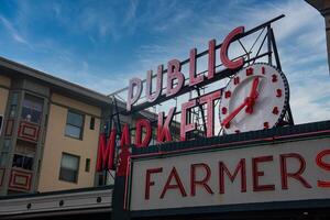 The iconic Pike Place Market sign with neon lettering, a large clock, and the word 'Farmers' visible, set against an urban building backdrop. photo