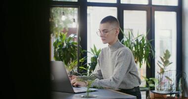 A young woman in casual clothes uses a laptop and makes notes in a notebook while sitting at a table in a cafe. Online learning, development and hobbies video