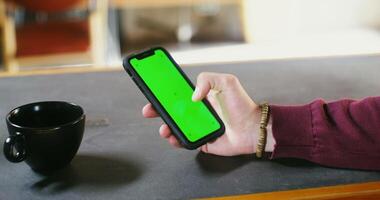 A man uses a phone with a green screen while sitting at a table. Male hand close-up, copy space, chroma key. video