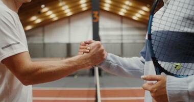 A close-up of a handshake between athletes after a tennis match through a net stretched in the middle of the court, the faces of the athletes are not visible video