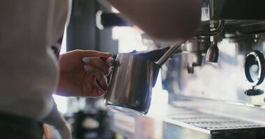 A woman pours warm cream into a decanter from a coffee machine. Close-up, no face in the frame, only female hands holding a jug to the tap of a coffee machine video