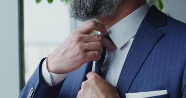 A man of European appearance with a beard, dressed in a business suit, straightens his tie, close-up, the man's face is not visible video