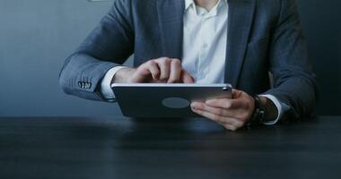 A young man of European appearance, dressed in a business suit, uses a tablet while sitting at a table in the office, close-up, the man's face is not visible video