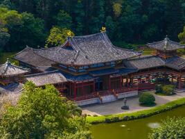 The Byodo In Temple in Oahu, Hawaii, features traditional Japanese architecture, vibrant red accents, a koi pond, and manicured gardens in a serene setting. photo