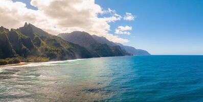 The Napali Coast on Kauai Island, Hawaii, features jagged cliffs with lush greenery, turquoise Pacific waters, pristine beaches, and scattered clouds. photo