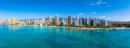 Aerial view of Waikiki Beach in Honolulu, Hawaii, with turquoise waters, high rise buildings, lush greenery, and Diamond Head crater in the background. photo