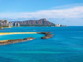 Turquoise waters, golden sands, and Honolulu's skyline frame Waikiki Beach, with Diamond Head Crater rising in the background under a clear sky. photo