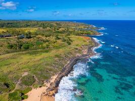 Aerial image of Kauai's coastline showing rugged cliffs, lush greenery, turquoise ocean waters, sandy beaches, and a clear sky with scattered clouds. photo