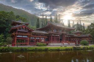 The Byodo In Temple in Oahu, Hawaii, surrounded by lush greenery, a serene pond, and dramatic mountains under a partly cloudy sky. photo