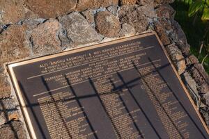 Plaque mounted on a stone structure honoring Ali i Aimoku Kaumuali i and Moi Wahine Kekaiha akulou, surrounded by greenery in an outdoor setting. photo