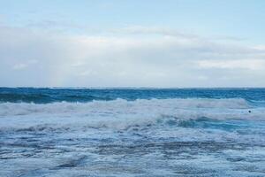 Waves Crashing on a Rocky Shoreline Under a Partly Cloudy Sky photo