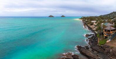 Aerial view of Lanikai Beach on Oahu Island, Hawaii, featuring turquoise waters, Mokulua Islands, lush greenery, sandy beaches, and rocky outcrops. photo