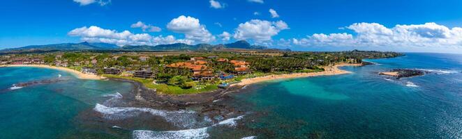 Aerial view of Kauai, Hawaii, showing golden beaches, turquoise waters, rocky outcrops, resorts with red tiled roofs, and the Napali cliffs in the background. photo