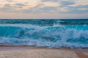 Dynamic ocean waves with white foam meet a sandy beach under a pastel sky, capturing the natural beauty of a coastal scene, possibly in Hawaii. photo