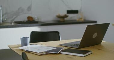 Architect's work desk equipped for remote work in a modern stylish kitchen, working papers and an open laptop stand on the kitchen table, no people in the video