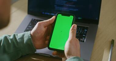 A young fair-skinned man scrolls the green screen of a mobile phone. Filming from behind, the man's face is not visible, chroma key, copy space video