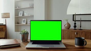 Close-up of an open laptop with a green screen standing on a table in a stylish home interior. A woman walks in the background with a smartphone in her hands. in 4k format, red komodo. video