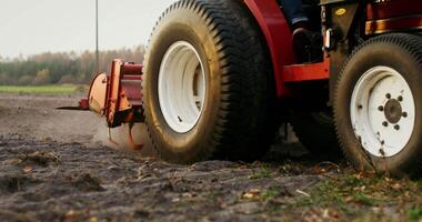 A close-up of the rear wheels of an agricultural tractor and a plow located at the rear of the machine, which lowers and begins to plow the field, there are no people in the video