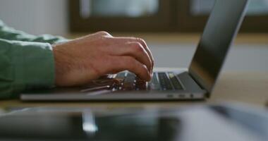 Young fair-skinned man typing text on laptop, male hands close-up, filming from the side, the man's face is not visible, unrecognizable person video