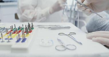 A dentist takes tool for examining a patient from a table with dental instruments laid out on it, a syringe with anesthesia, scissors and nozzles for a drill machine, close-up. in 4k, red komodo video