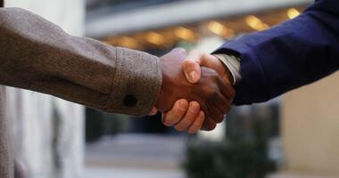Two men of different nationalities shake hands while standing outdoors near city buildings, men's hands are close-up, faces are not visible. in 4k, red komodo video