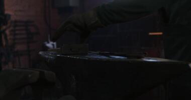 A blacksmith in protective gear takes one hammer from the anvil and lays down another, close-up, no face. Working process of forging iron in detail. 4k , red komodo video