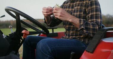 Young black-haired male tractor driver with a beard eating a sandwich sitting in the open cabin of a modern agricultural machine, close-up of a man's hands, the face is not visible video