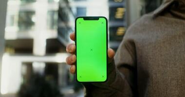 Close-up of a mobile phone with a screen forward in the hands of a young man, no face. Copy space, green screen, chroma key, mockup. in 4k, red komodo video
