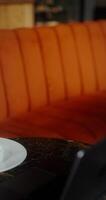 A woman takes a glass of ice coffee from the table while sitting at the table opposite an open laptop. Close-up of the table, no face video