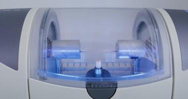 CNC dental machine makes a dental implant by rotating, polishing and flushing with water streams, close-up view, modern dental technology. in 4k, red komodo video