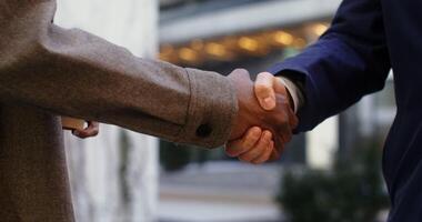 Two men of different nationalities shake hands in informal communication, standing outdoors, men's hands are close-up, faces are not visible. in 4k, red komodo video