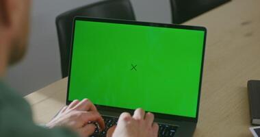 uma jovem pele clara homem é digitando em uma computador portátil com uma verde tela. filmando a partir de atrás, a do homem face é não visível, croma chave, cópia de espaço video