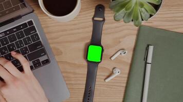 Close-up of a digital clock with a green screen lying on a table next to female hands typing on a laptop. Chroma key, mockup, copy space. in 4k format, red komodo. video