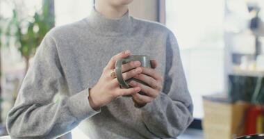 Young european woman, dressed in casual clothes, drinking coffee while sitting at a table in a cafe, female hands with a mug close-up, no face visible video