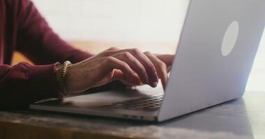 A fair-skinned man in casual clothes is typing on a laptop, sitting at a table, close-up. Male hands with a bracelet, no face visible video