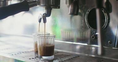 A professional coffee machine pours coffee in a thin stream simultaneously into two glasses, close-up, there are no people in the video