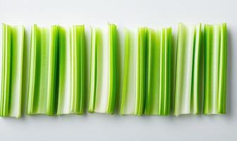 A row of celery sticks are lined up on a white surface photo