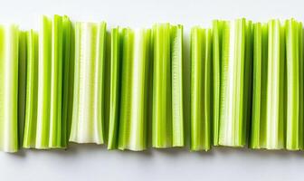 A row of celery sticks are lined up on a white background photo