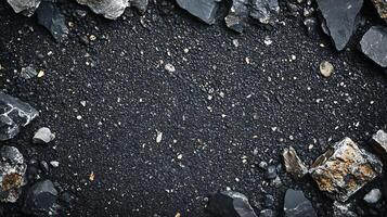 Gritty black surface with scattered stones and larger rocks framing the edges creates a dark, textured backdrop. Raw and rugged look. photo
