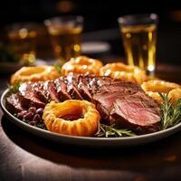 A plate of sliced meat with Yorkshire pudding and rosemary on a table with drinks photo