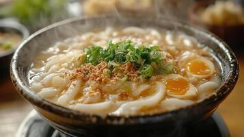 A steaming bowl of udon noodles in a savory broth, topped with green onions and other ingredients. photo