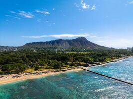 Aerial view of Waikiki Beach in Oahu, Hawaii, with Diamond Head Crater, turquoise waters, sandy shoreline, beachgoers, and a breakwater visible. photo