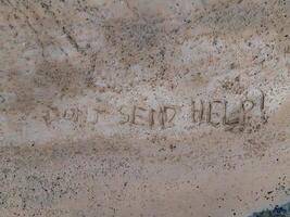 A sandy area features the message 'DON'T SEND HELP ' etched prominently, surrounded by scattered pebbles and debris, suggesting a coastal setting. photo