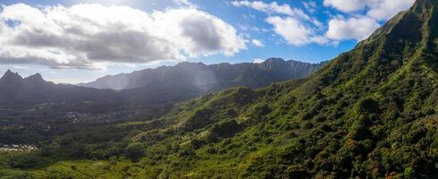 Lush green mountains and valleys of the Ko olau Range on Oahu Island, Hawaii, with sunlight filtering through clouds and a settlement in the valley. photo