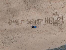 An aerial view of a sandy beach on Kauai island featuring the phrase 'DON'T SEND HELP ' written in the sand, with a person lying nearby. photo