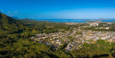 Aerial view of a residential area on Oahu island, Hawaii, with green mountains, the Pacific Ocean, small islands, and a bright blue sky in the background. photo