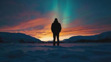 A person standing in the snow at sunset with the aurora borealis photo
